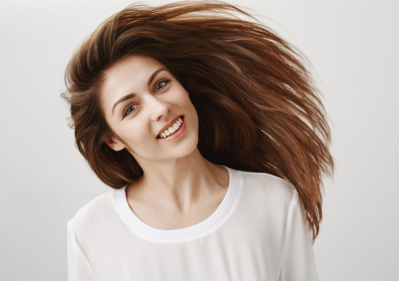 Happy people are beautiful. Portrait of attractive young caucasian brunette waving head and smiling broadly, being satisfied with shampoo that straighten hair strands, standing over gray background